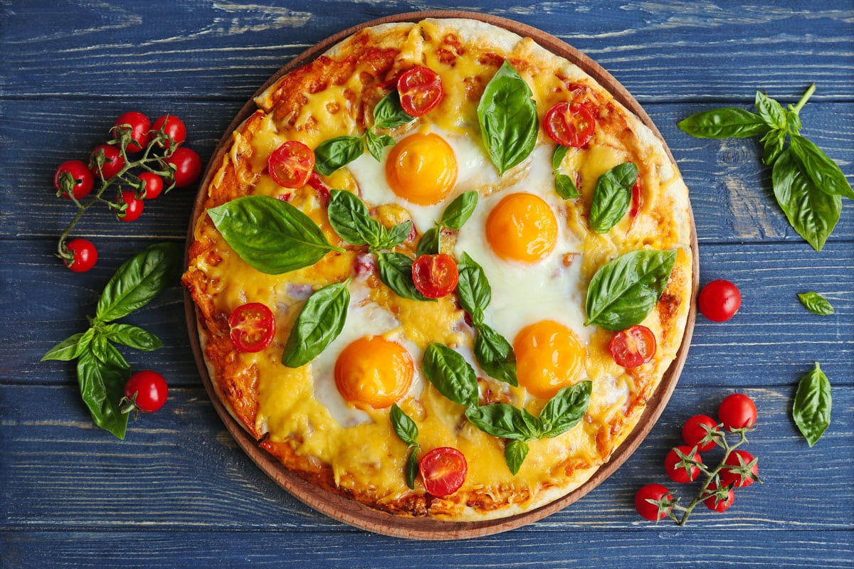 Margarita pizza with basil leaves and egg on wooden table
