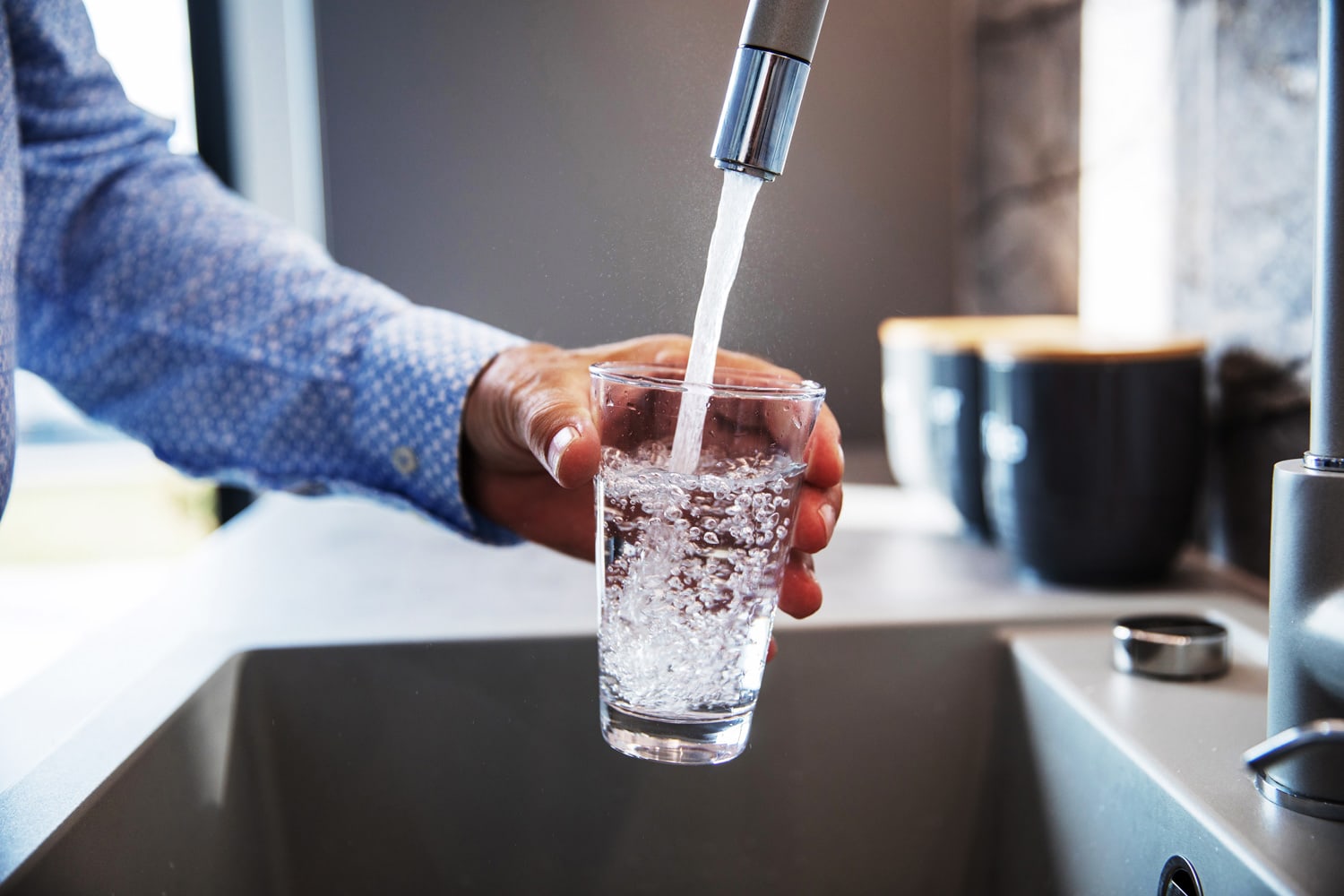 Mature male hand pouring a glass of water from tap in the kitchen sink