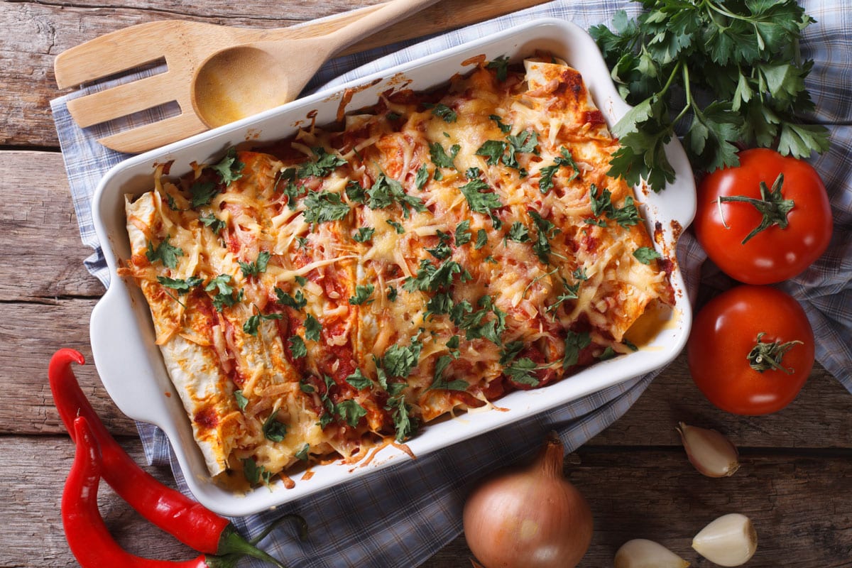 Mexican enchilada in a baking dish with the ingredients on the table