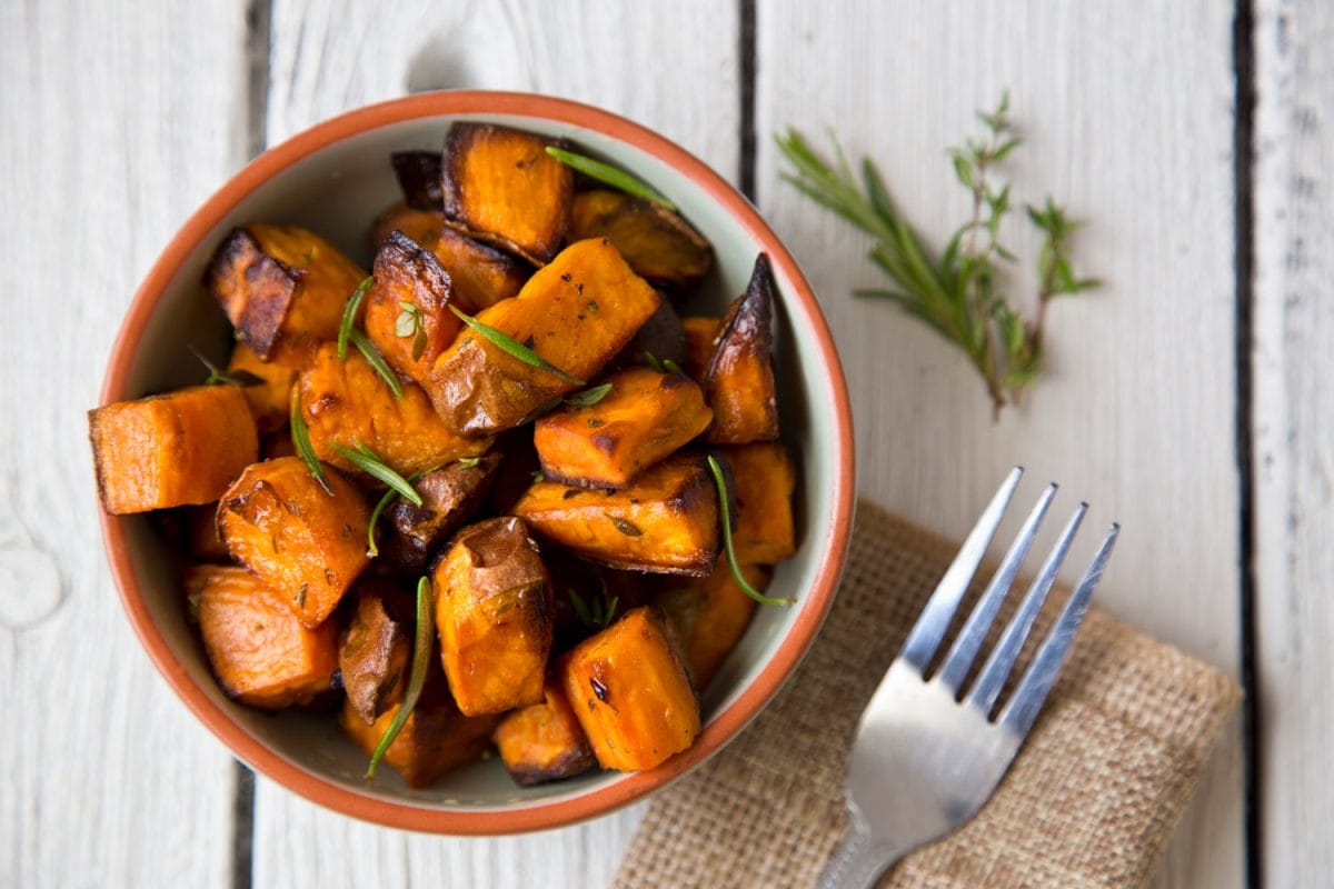 Oven baked sweet potatoes drizzled with oregano on the table