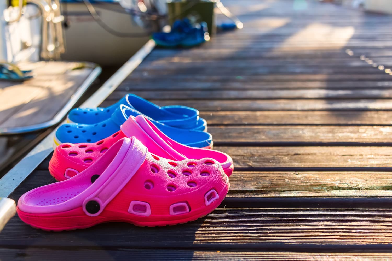 Pink and blue flip flops on the wooden pier with blurred sun glare