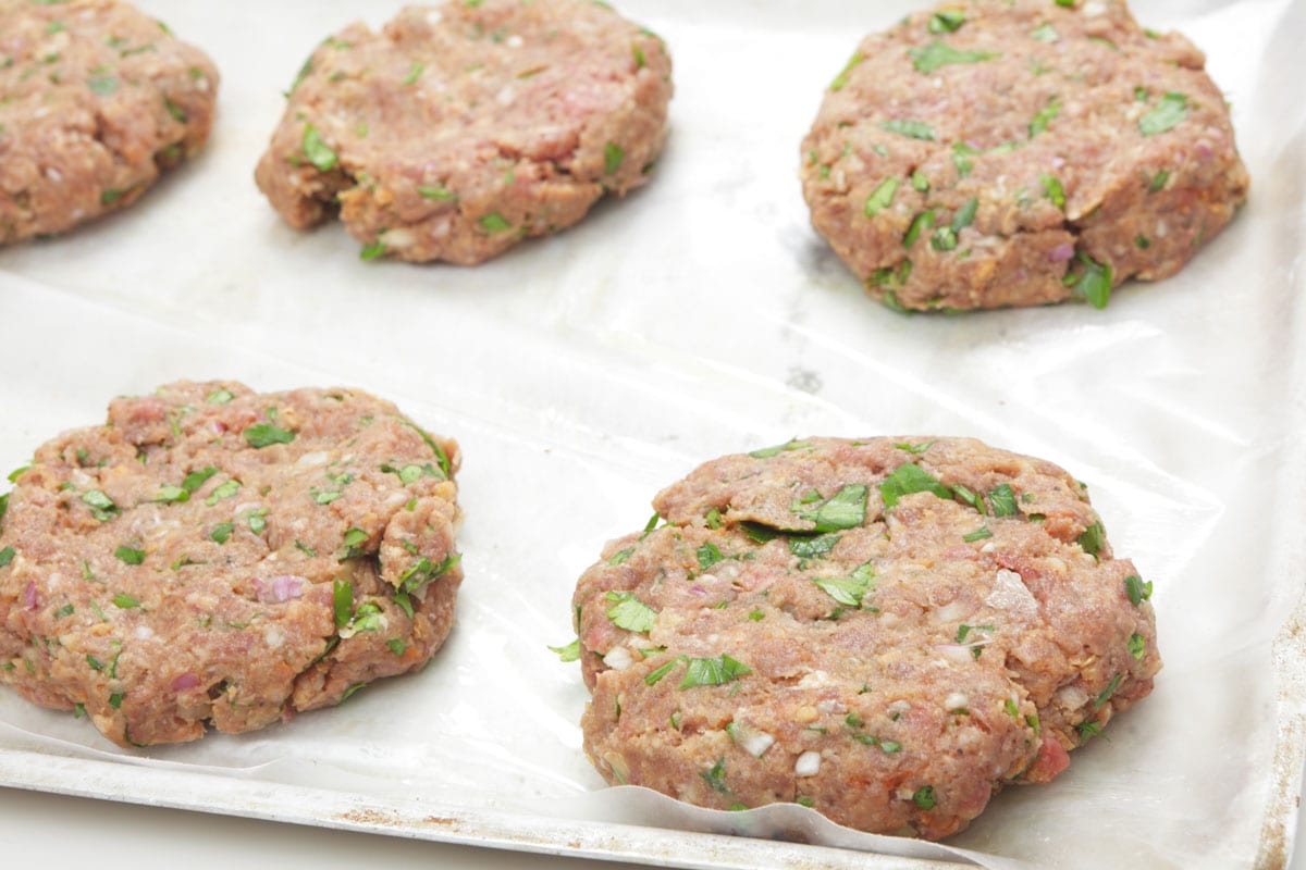 Raw beeburger beef patties on a oiled greaseproof paper on a baking sheet