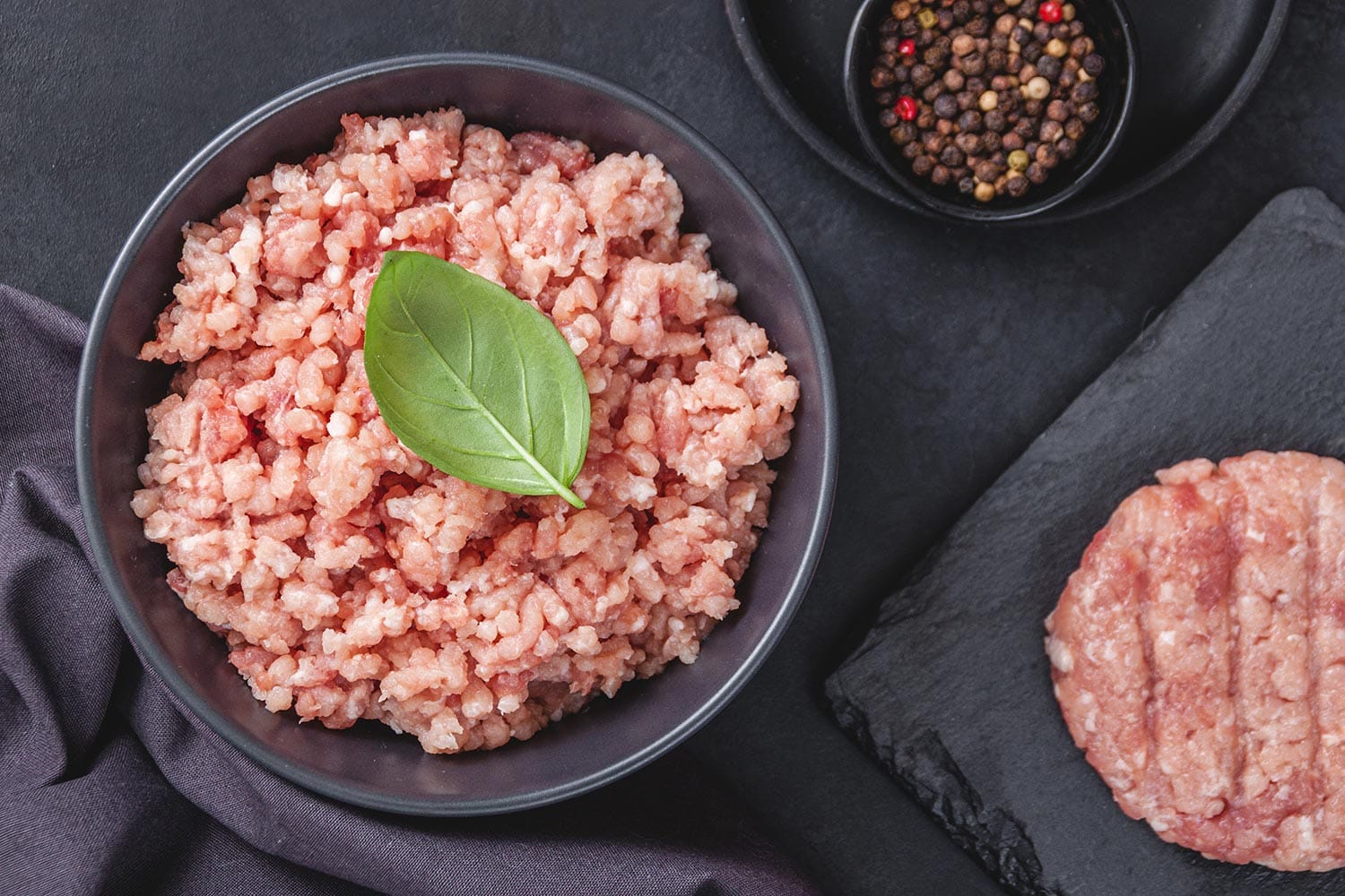 Raw minced meat in bowl on black stone table and ingredients.