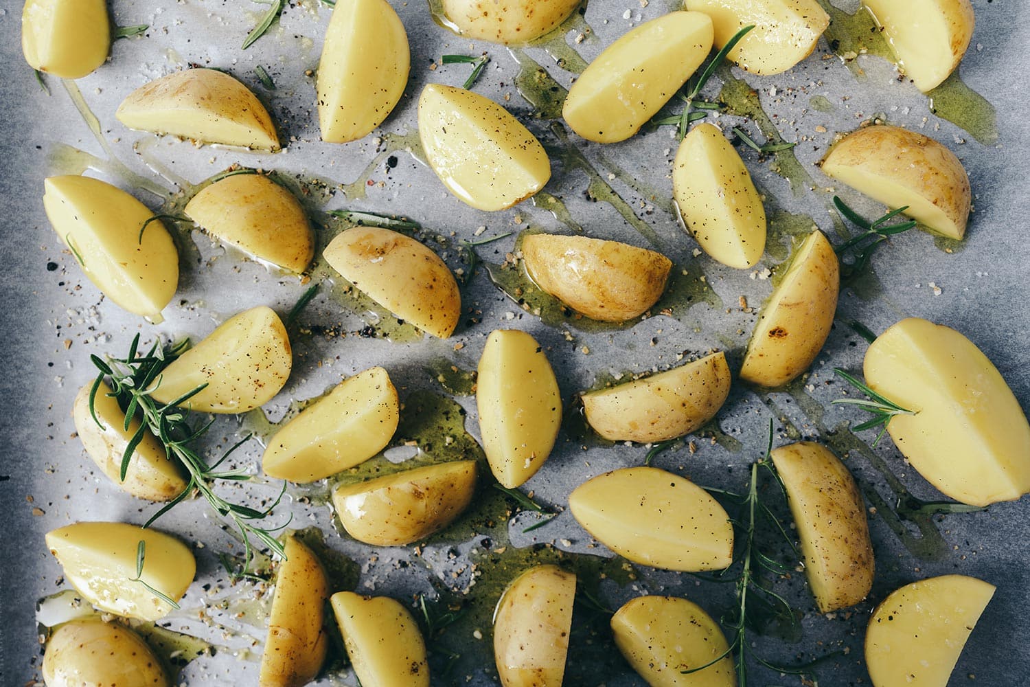 Raw potato wedges with oil and pepper on baking tray