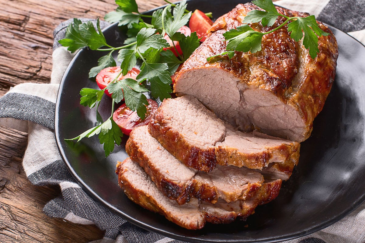 Roast pork with herbs and vegetables on rustic wooden table