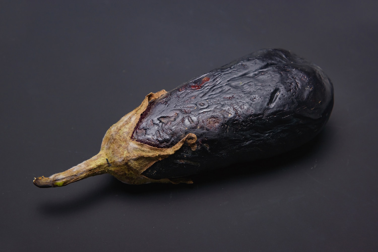 Spoiled aubergine on a black background. Mold on the eggplant.