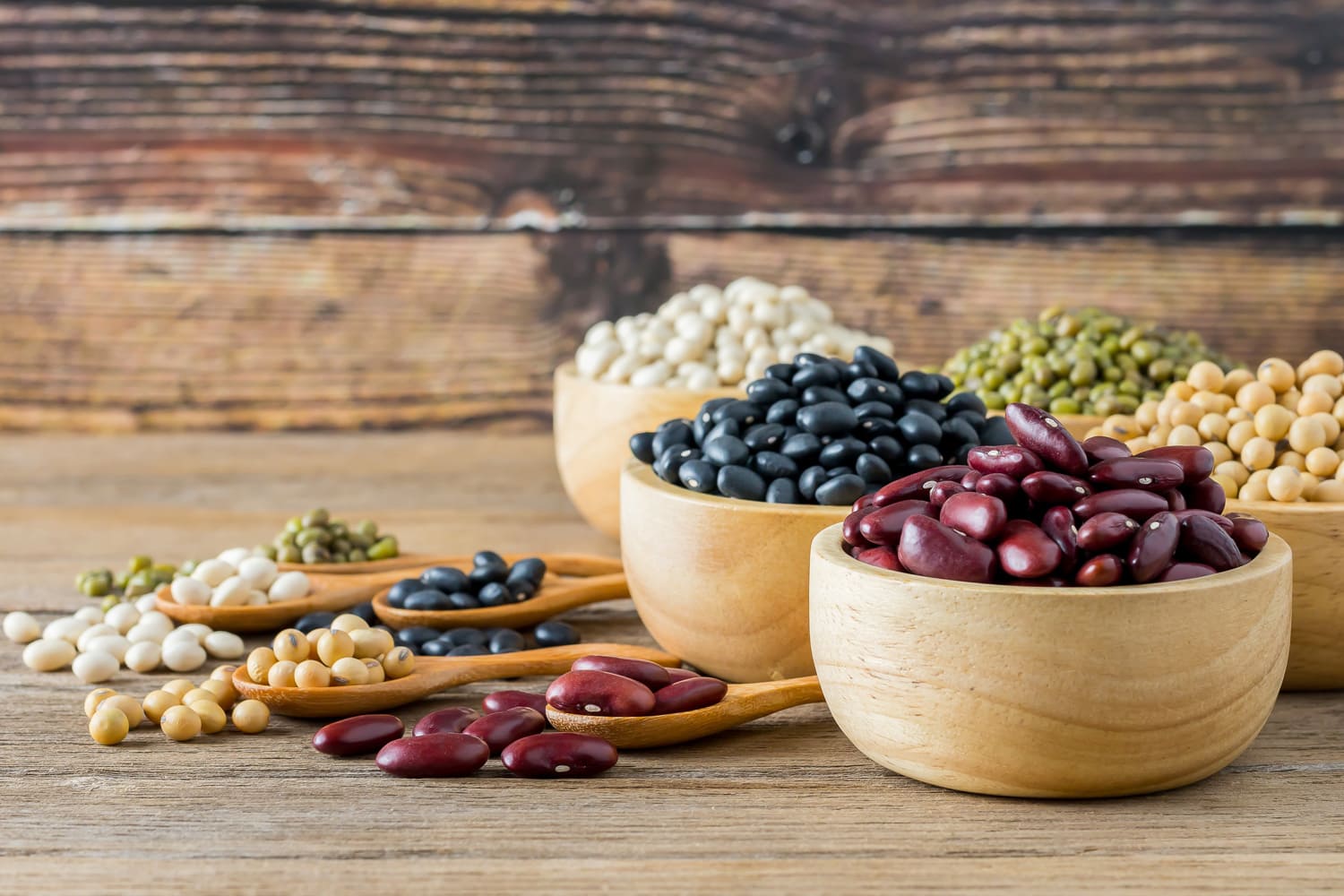 Various grains such as soybeans, black beans, red beans, dried corn in a wooden cup on a wooden table background.