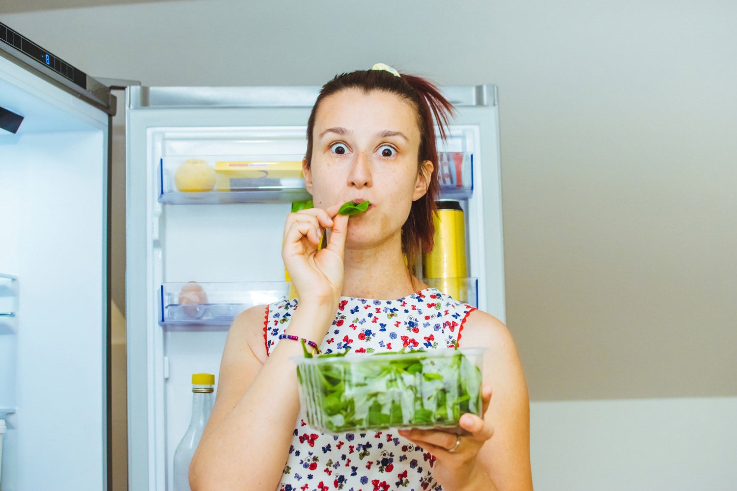 Woman eating salad near refrigerator stock photo
