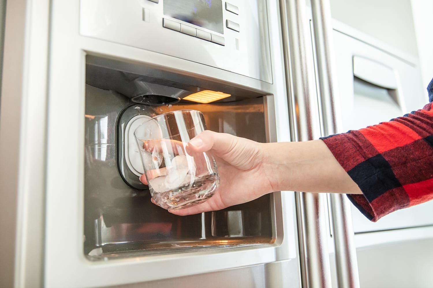 Woman's hand holds glass and uses refrigerator to make fresh clean ice cubes