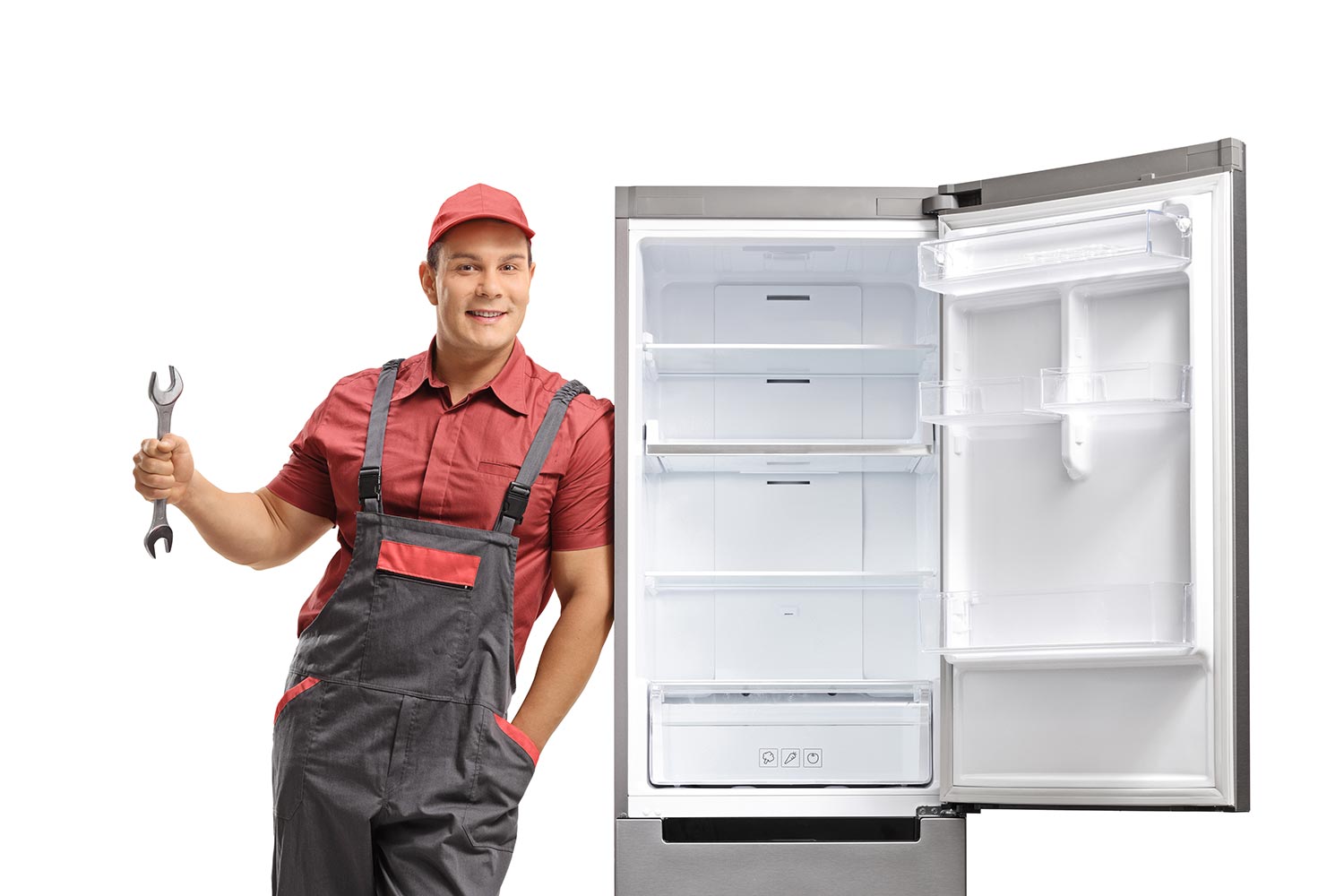 Young repairman holding a wrench and leaning against an empty fridge