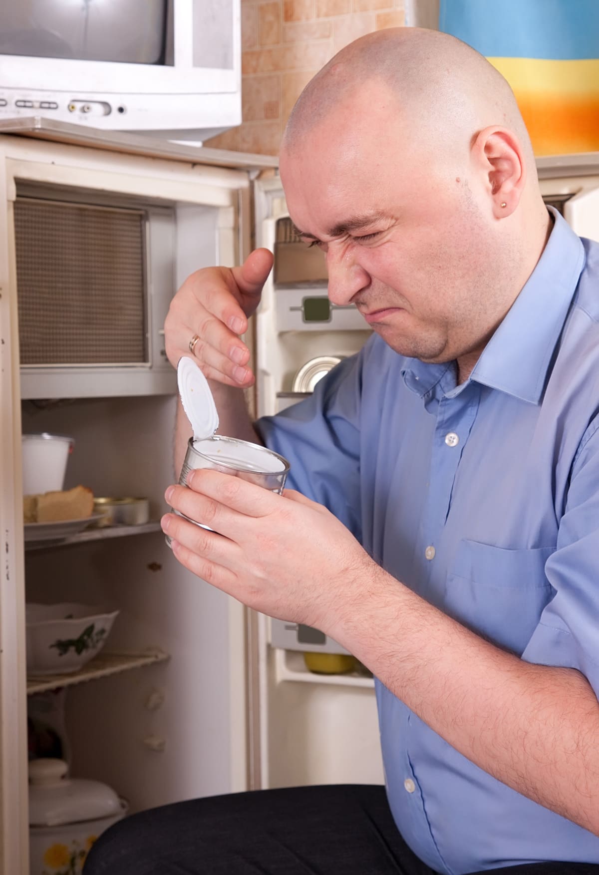 man holding her nose because of bad smell from food near refrigerator at home