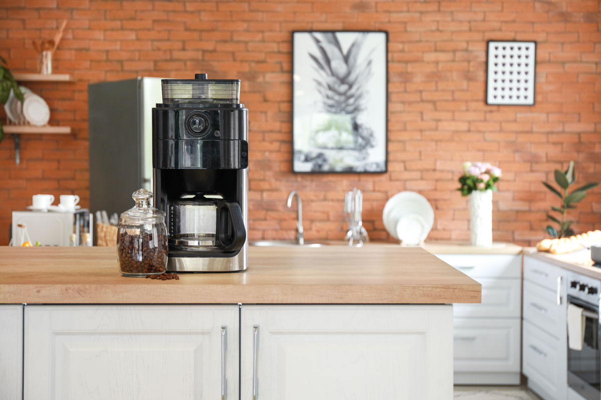 A small coffee machine on top of a wooden countertop inside a rustic kitchen