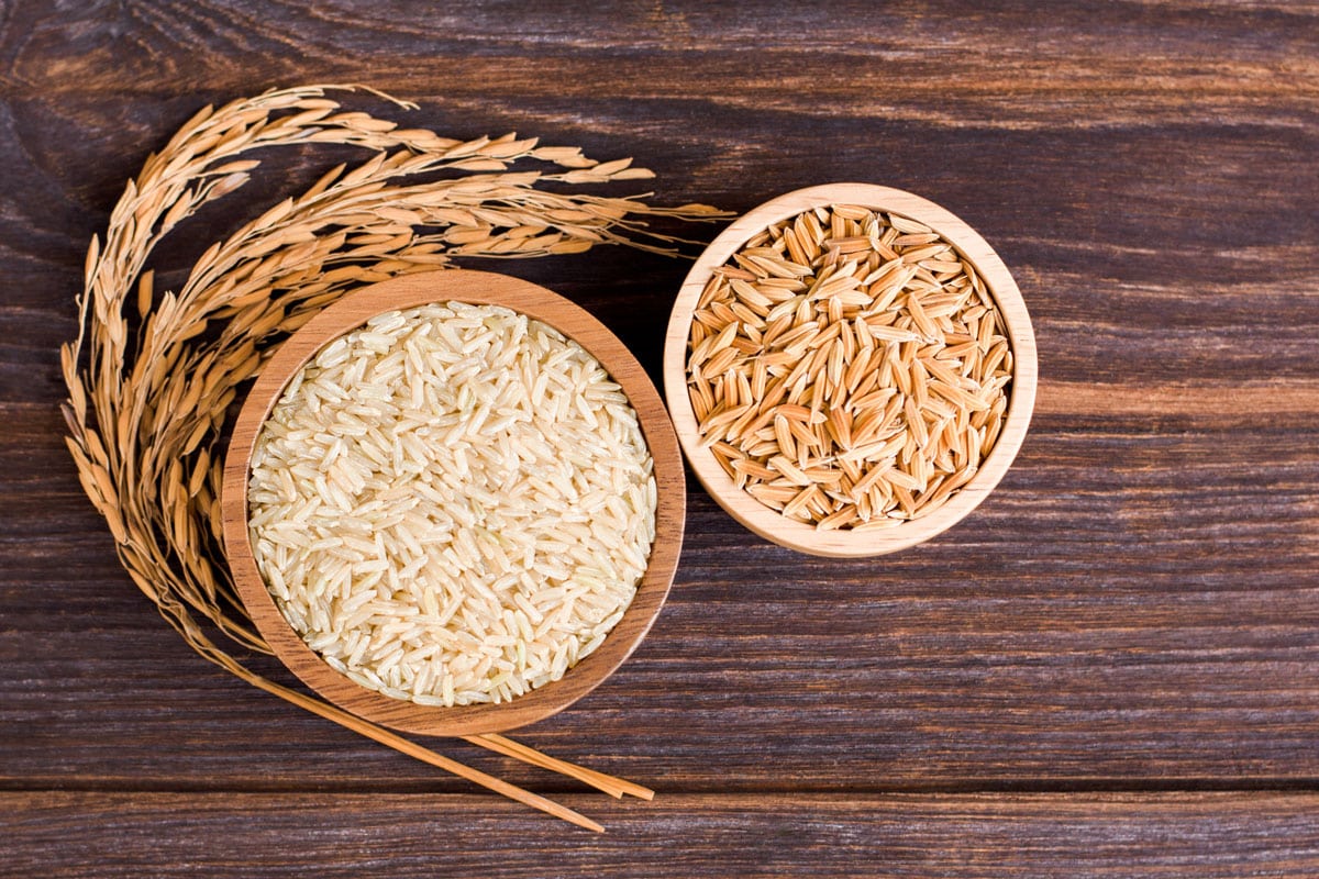 Brown rice, natural long rice grains (Thai jasmine rice) and paddy rice in wooden bowl isolated on wooden table