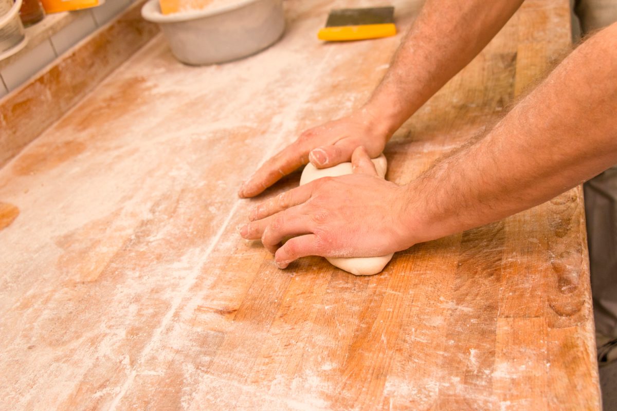 Hands of a baker kneading bread dough on a flour sprinkle worktable