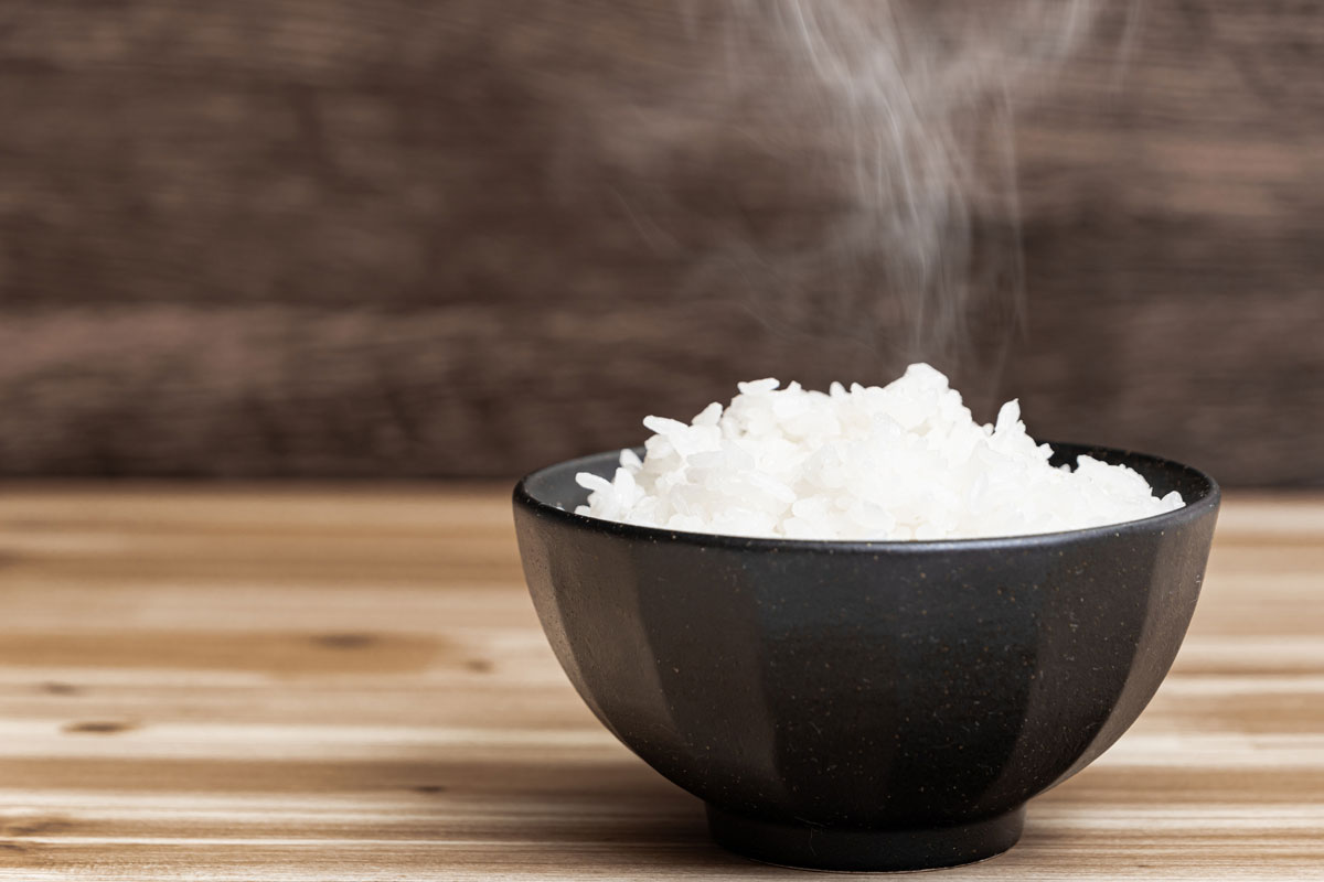 Hot Japaneses white rice in a black bowl on a wooden light desk