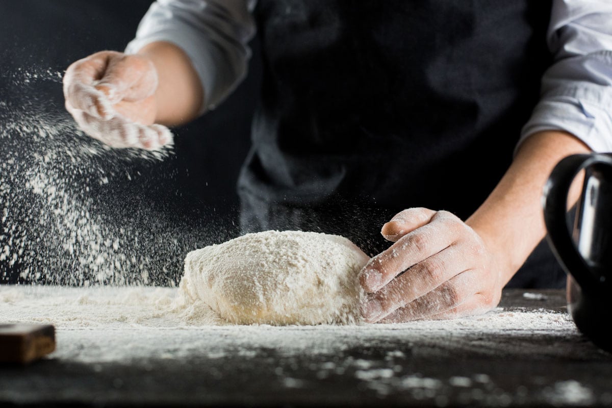 Pastry chef adding adding flour to the dough
