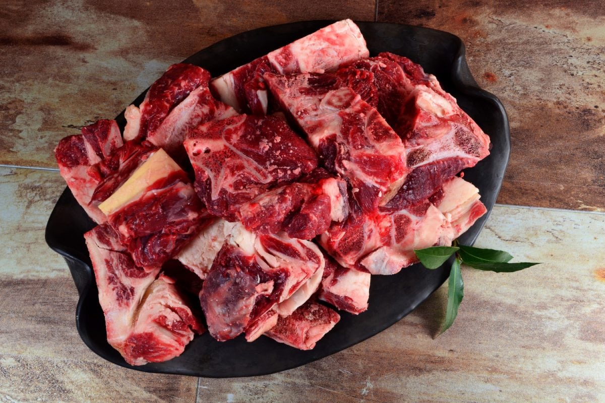 Raw meat with bone on clay plate and brown stone background.Raw meat with beef bone. Beef bone selection for soup