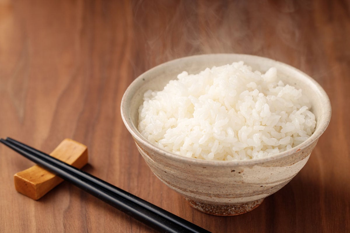 Steaming white hot rice on a white bowl with black chopstick on wooden desk
