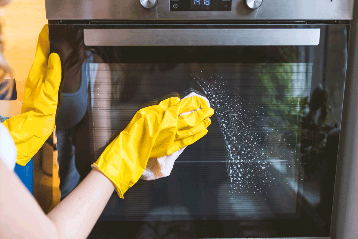 female hand with yellow protective gloves cleaning oven door. How To Clean An Oven With a Blue Interior (Lg Or Kitchenaid)