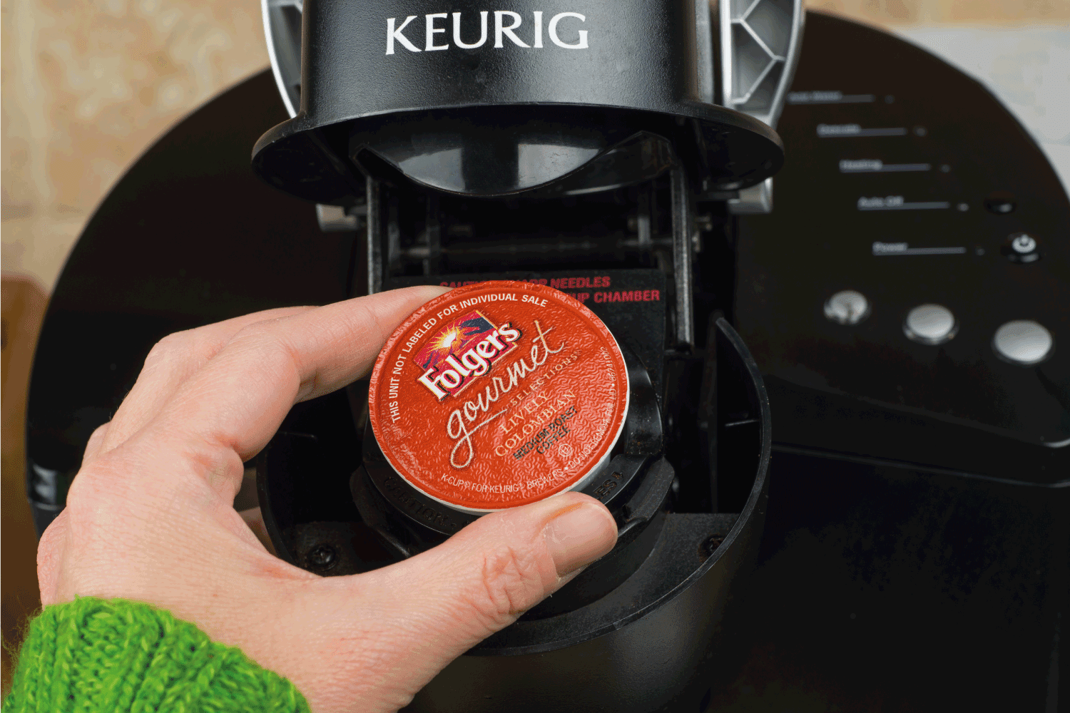woman inserting single-serve K-cup Foldger's coffee into a Keurig coffee maker.