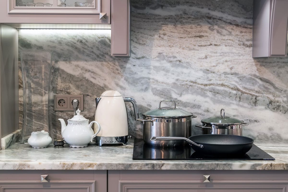 A marble kitchen countertop filled with lots of pots, kettles and other kitchen utensils