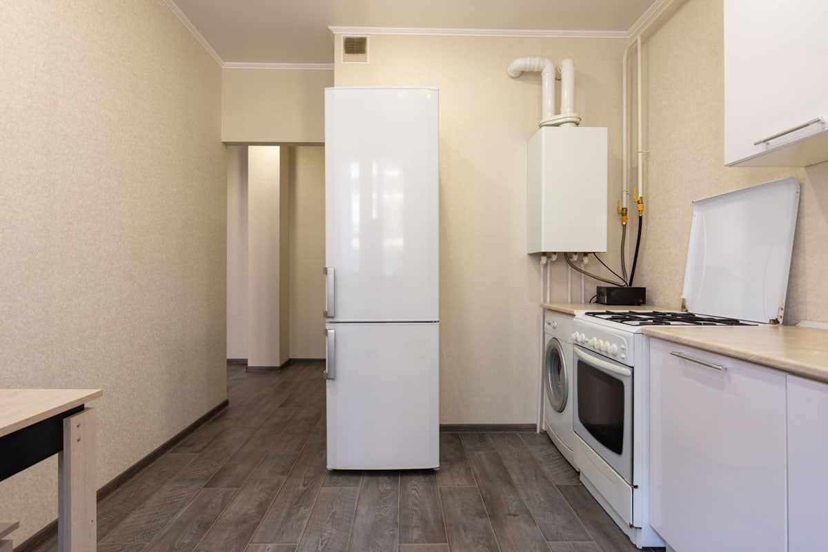A small white refrigerator inside a narrow beige living room