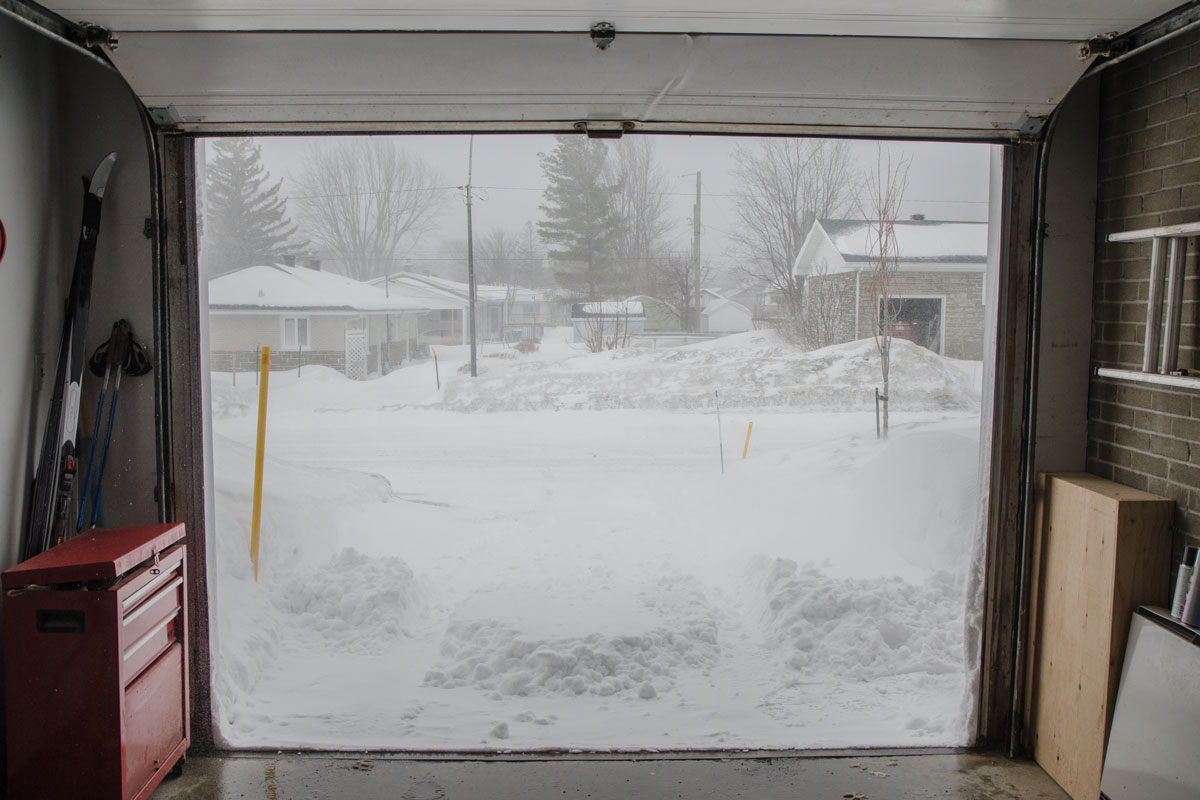 An opened garage door showing heavy snowfall outside the house