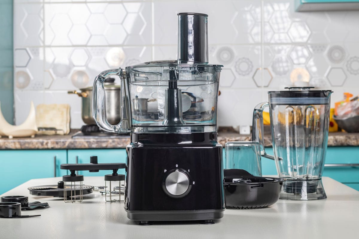 Black food processor and other accessories on it on a white countertop