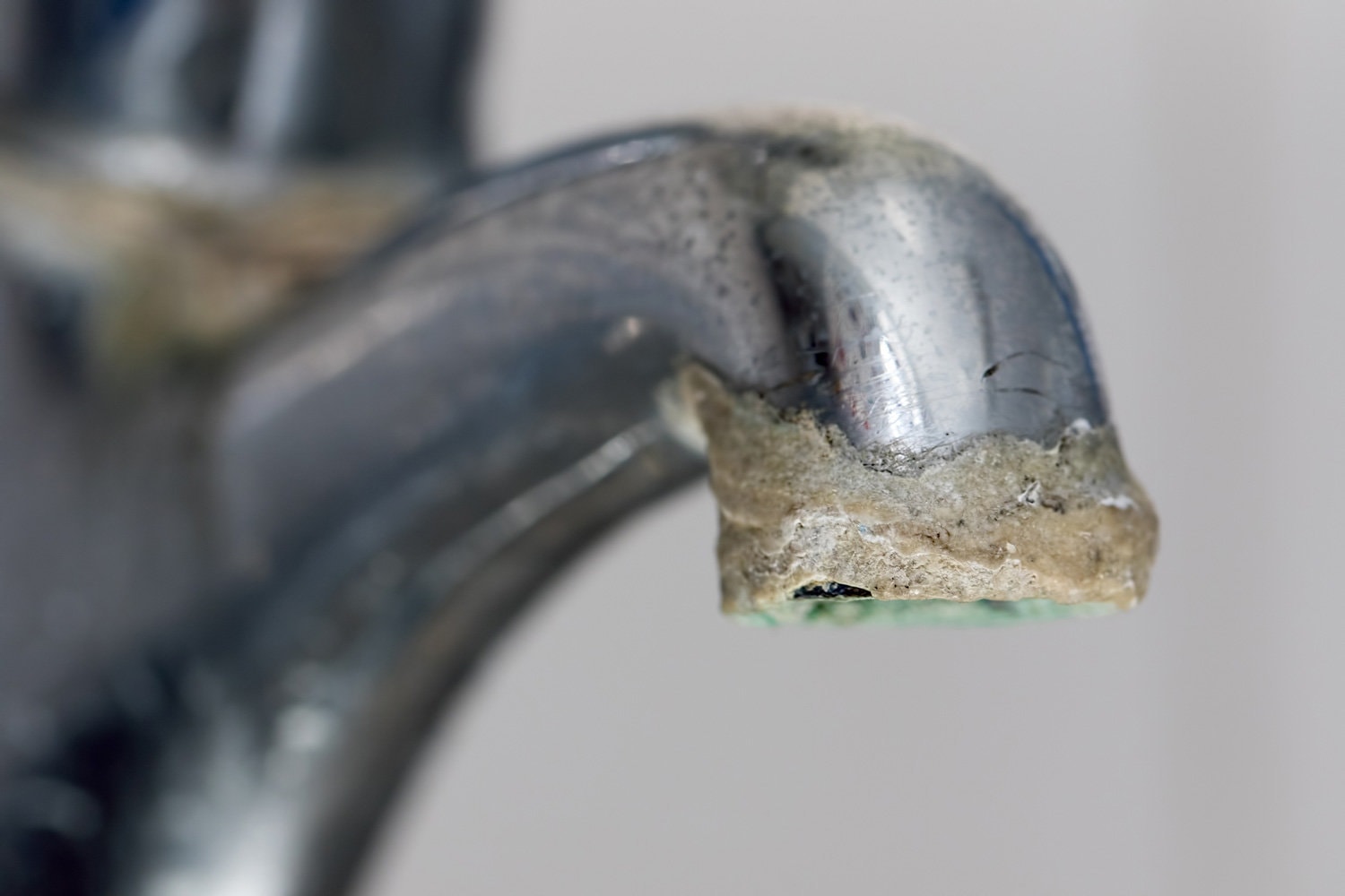 Close-up of limescale build-up. Selective focus on hard water deposit on old tap spout. Chrome kitchen or bathroom faucet with crusty calcium carbonate needing descaler.