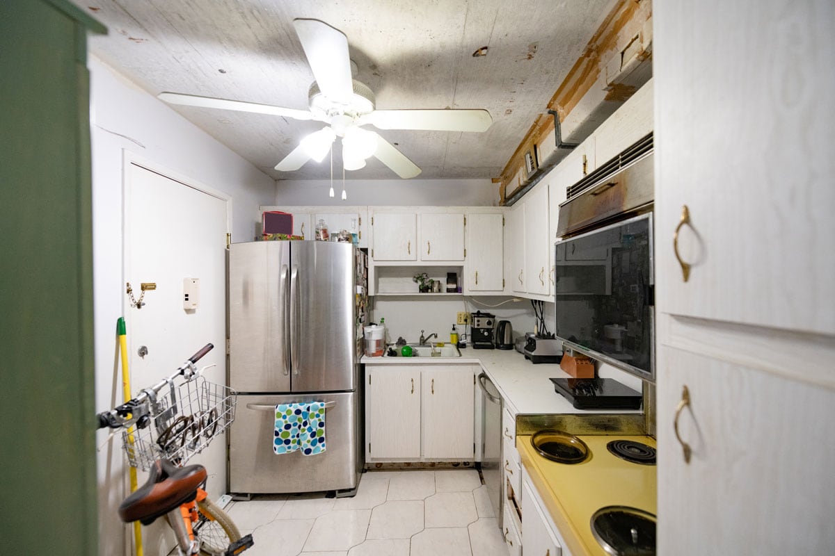Interior of a small apartment kitchen with white painted walls and cabinets and refrigerator on the side