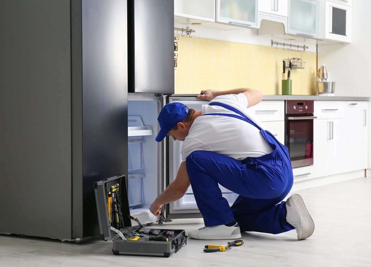 Male technician repairing broken refrigerator in kitchen