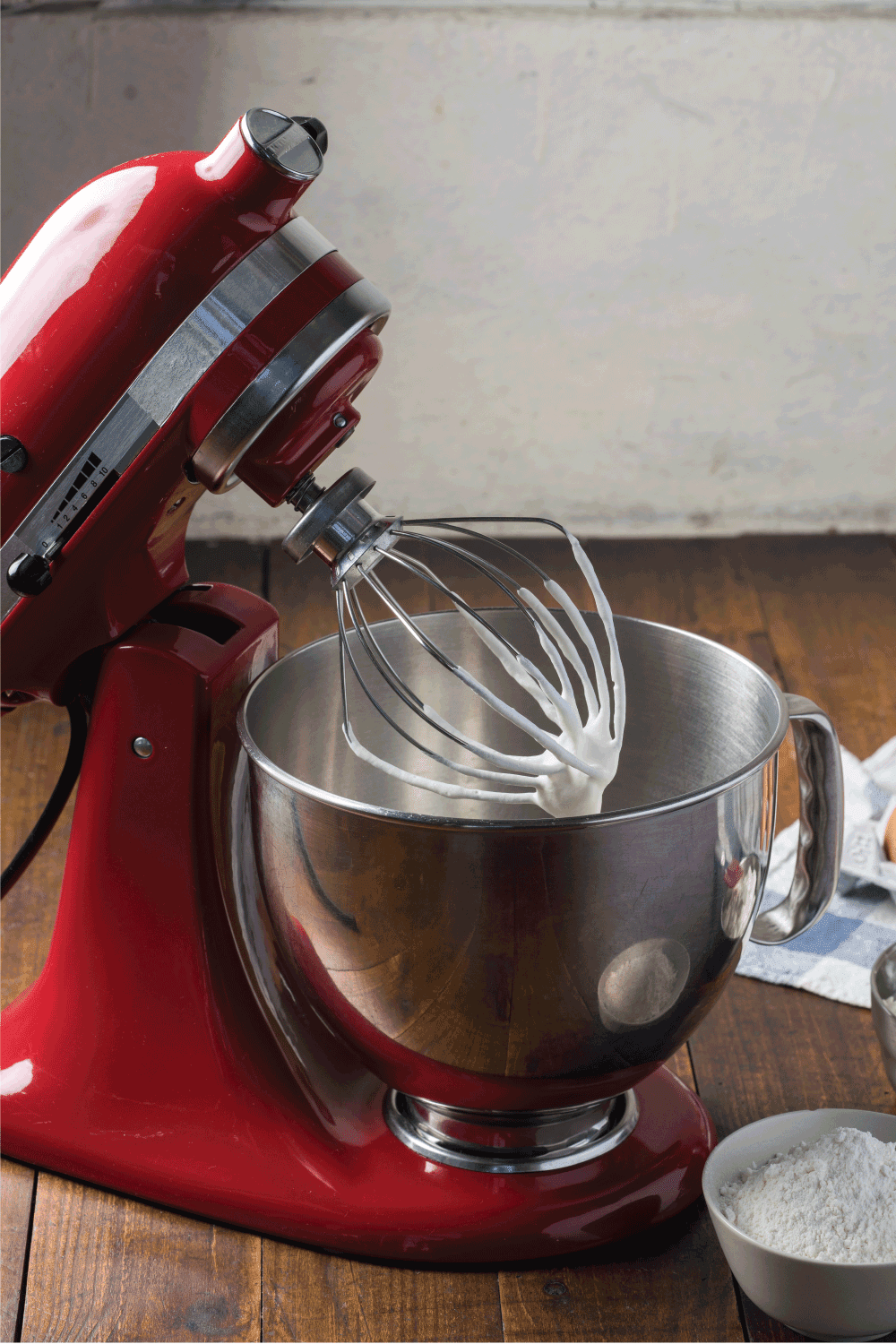 Standing mixer with cream on whisk on wooden table with ingredients