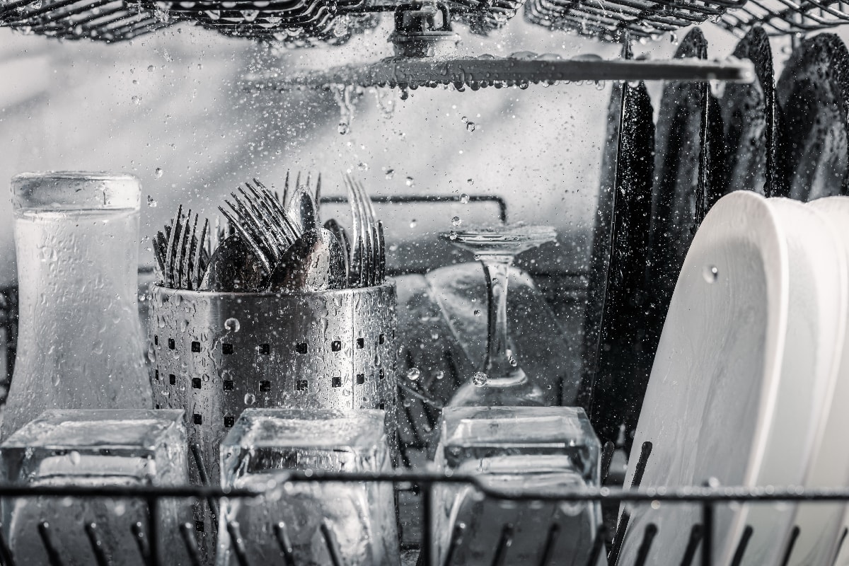 Transparent and black and white dishes as well as cutlery and glasses are washed in the dishwasher
