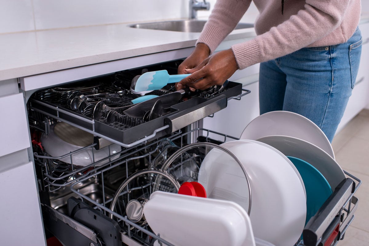 a woman's hands holding a spatula, taking out clean cutlery from the dishwasher rack