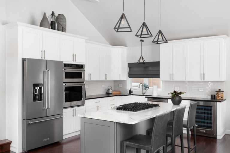 beautiful white kitchen in a modern farmhouse with black lights hanging from the vaulted ceiling over the island bar stools and KitchenAid steel appliances, KitchenAid Refrigerator Not Cooling - What To Do?
