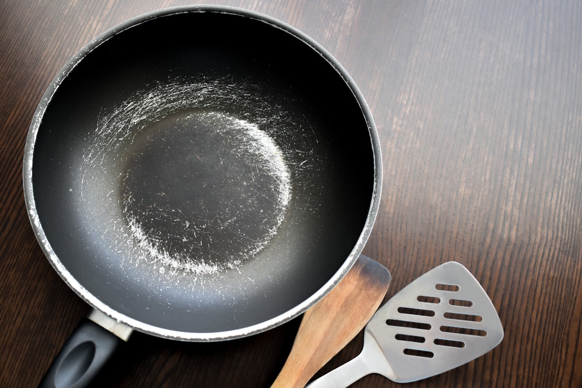 A non stick skillet with a wooden and stainless steel spatula on the side