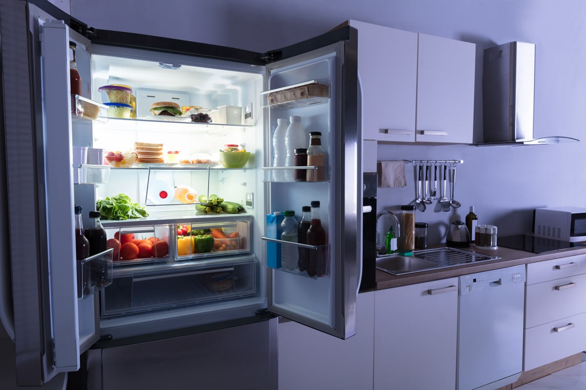 A refrigerator filled with vegetables and fruits inside left open