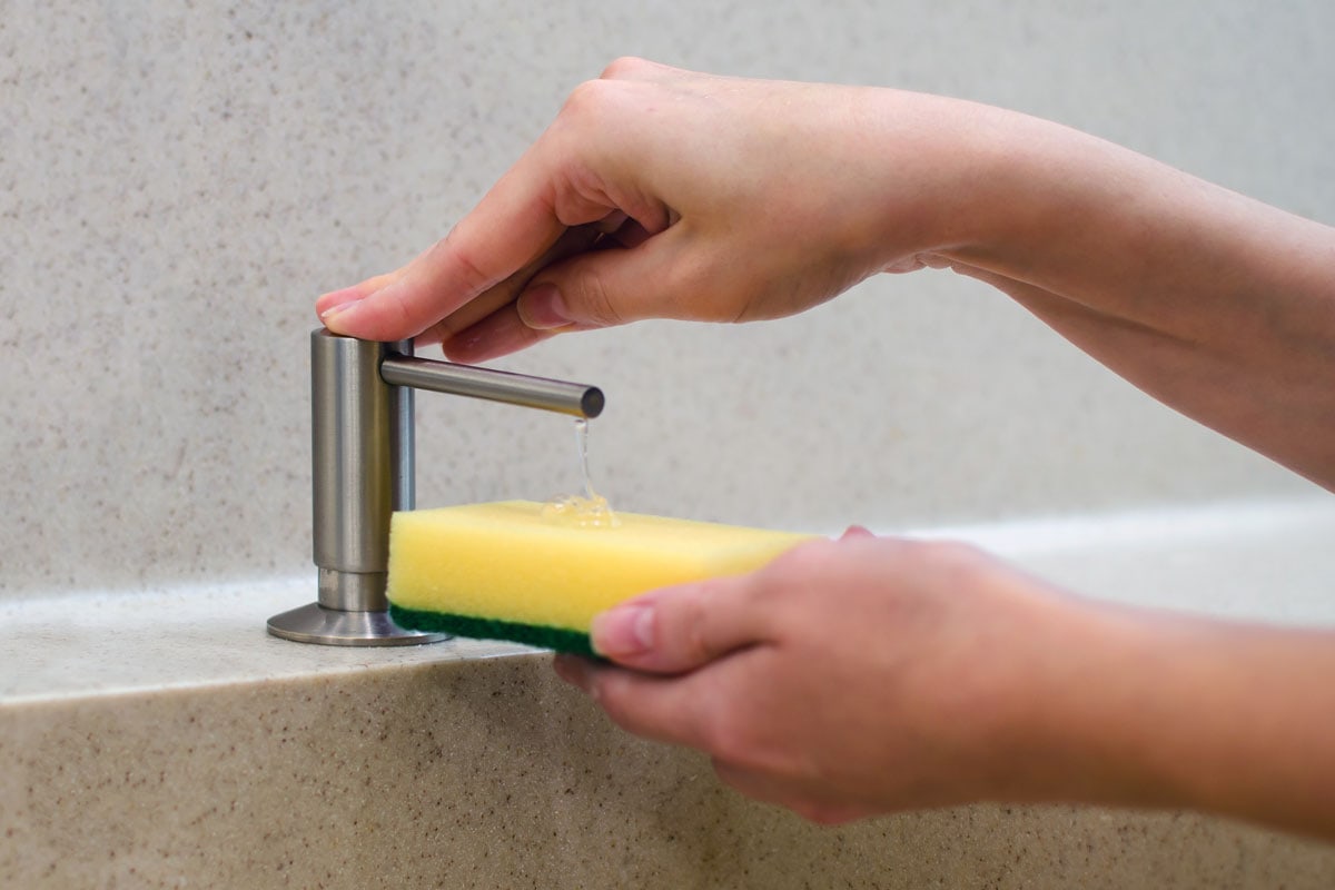 A woman uses a liquid soap dispenser in the kitchen, a sponge for washing dishes