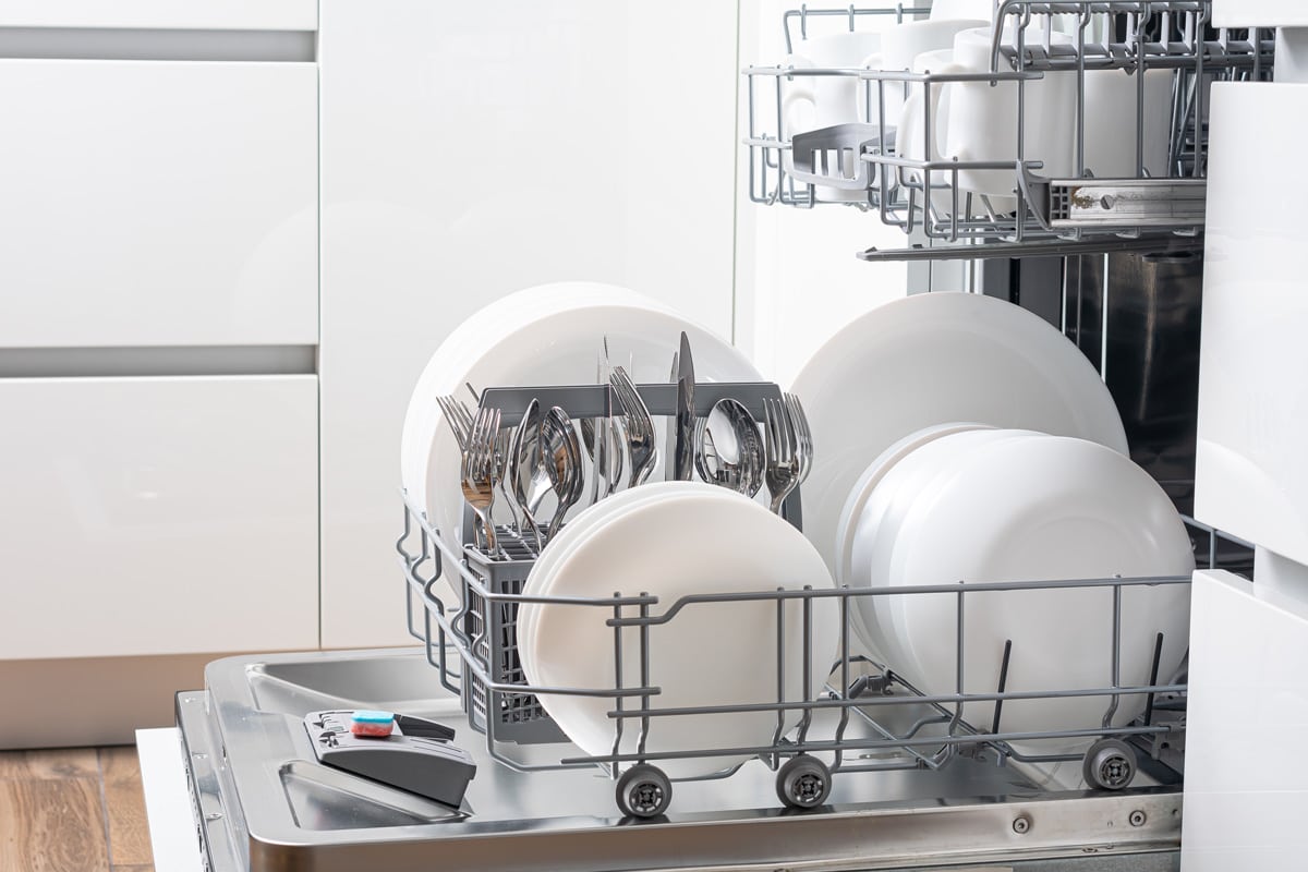An opened dishwasher with lots of plates and other kitchen utensils