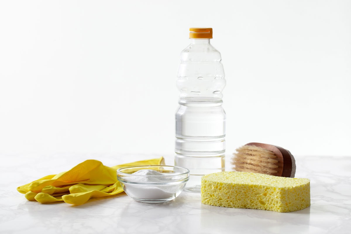Baking soda, a bottle of vinegar, rubber gloves on a marble surface