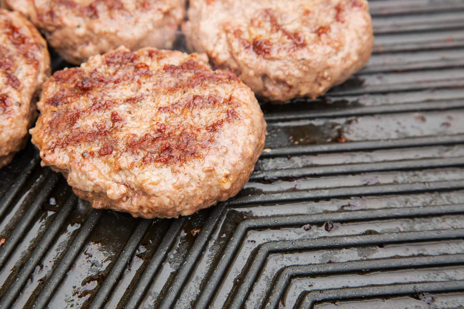 Beef burgers cooking on a metal griddle — Photo