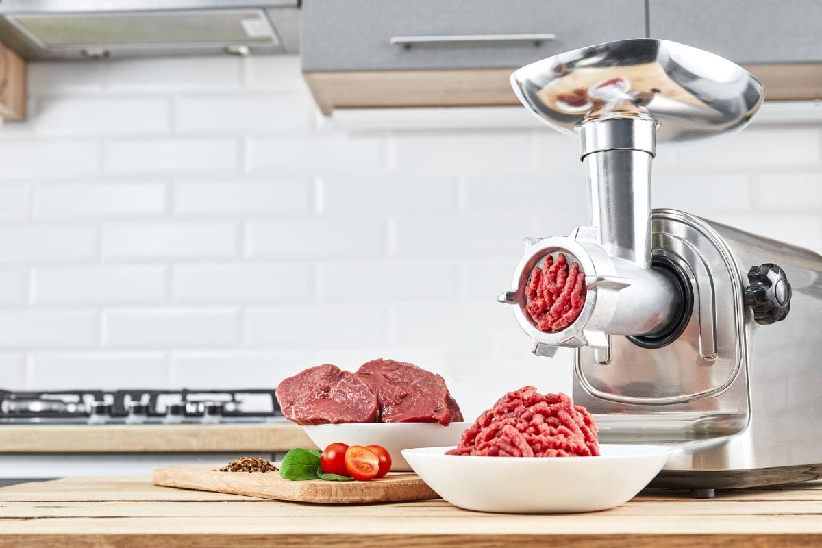Bowl of mince with electric meat grinder in kitchen interior