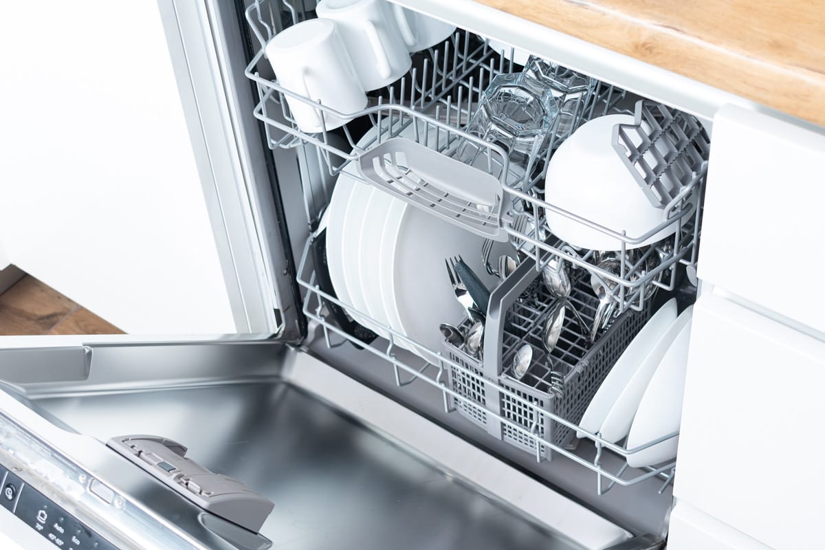 Dishwasher left open in the kitchen filled with lots of dishes and utensils