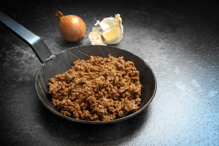 fried ground beef with onion and garlic in a black pan on a dark stone background with copy space, selected focus, narrow depth of field, What If You Don't Drain Ground Beef While Cooking?