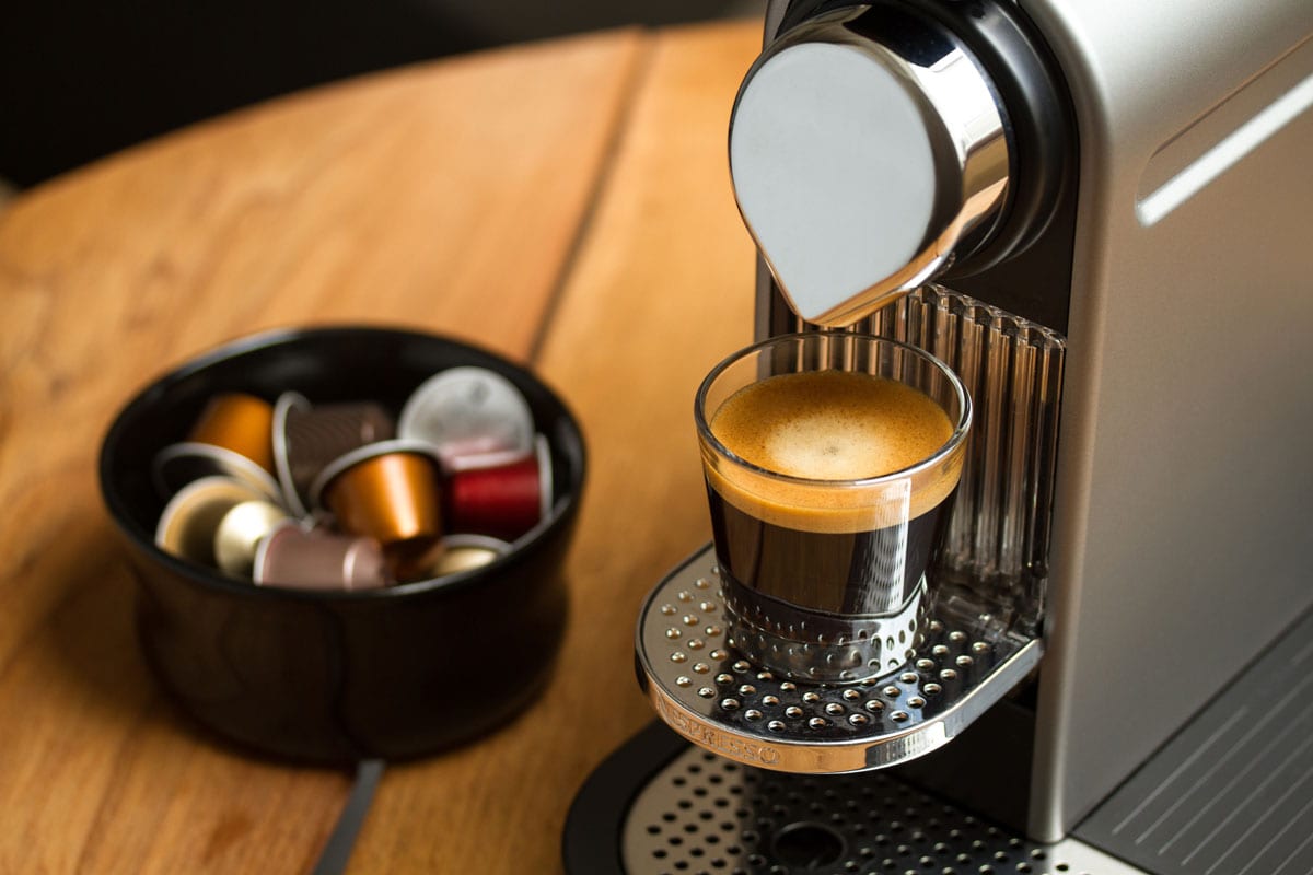 Freshly brewed espresso in glass standing on silver Nespresso coffe machine