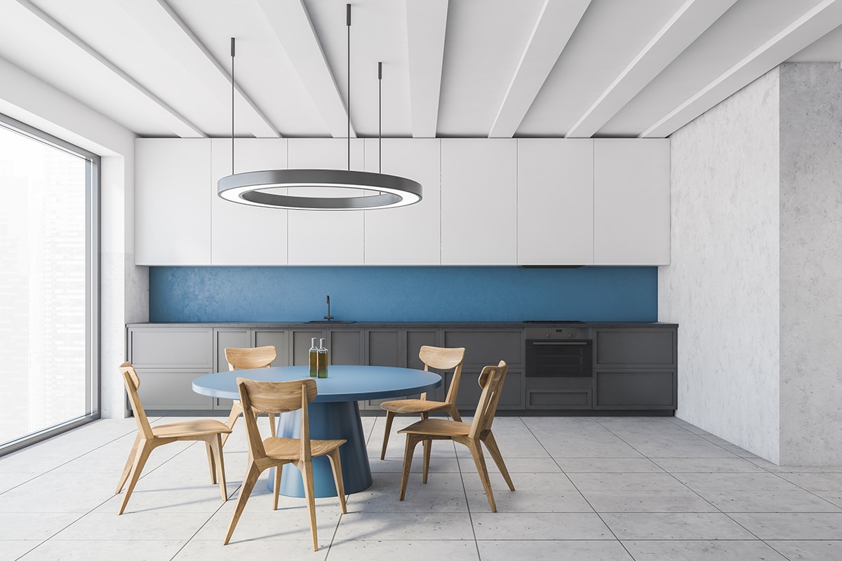Interior of modern kitchen with white and blue walls, tiled floor, gray cupboards and round dining table with chairs
