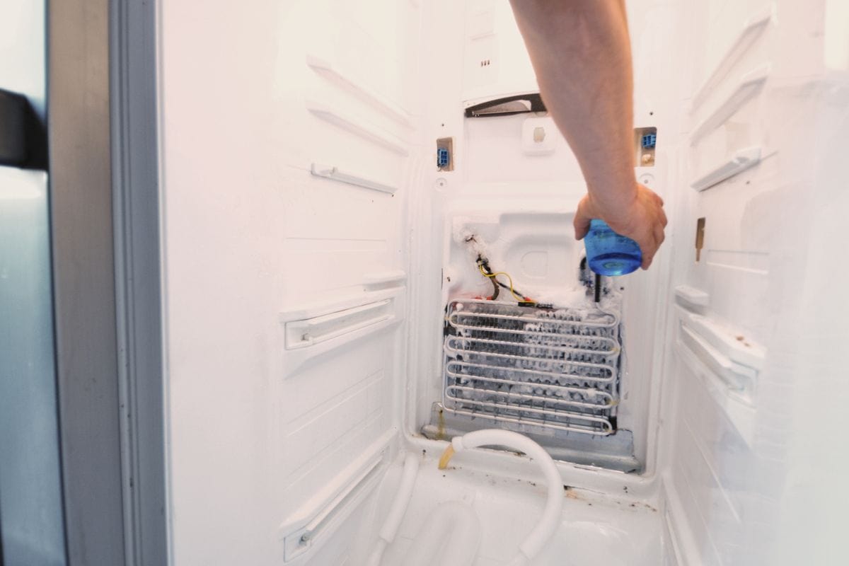 "Man's hand repairing fridge, pouring hot water over completely iced up element to thaw it quicklymore fridge repair shots"