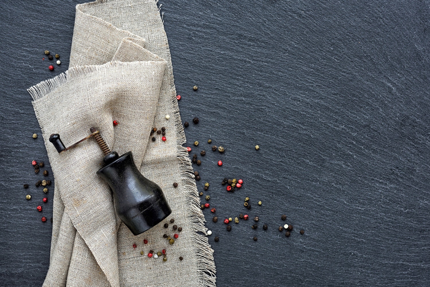 Mixed peppercorns and vintage mill on a slate board, top view