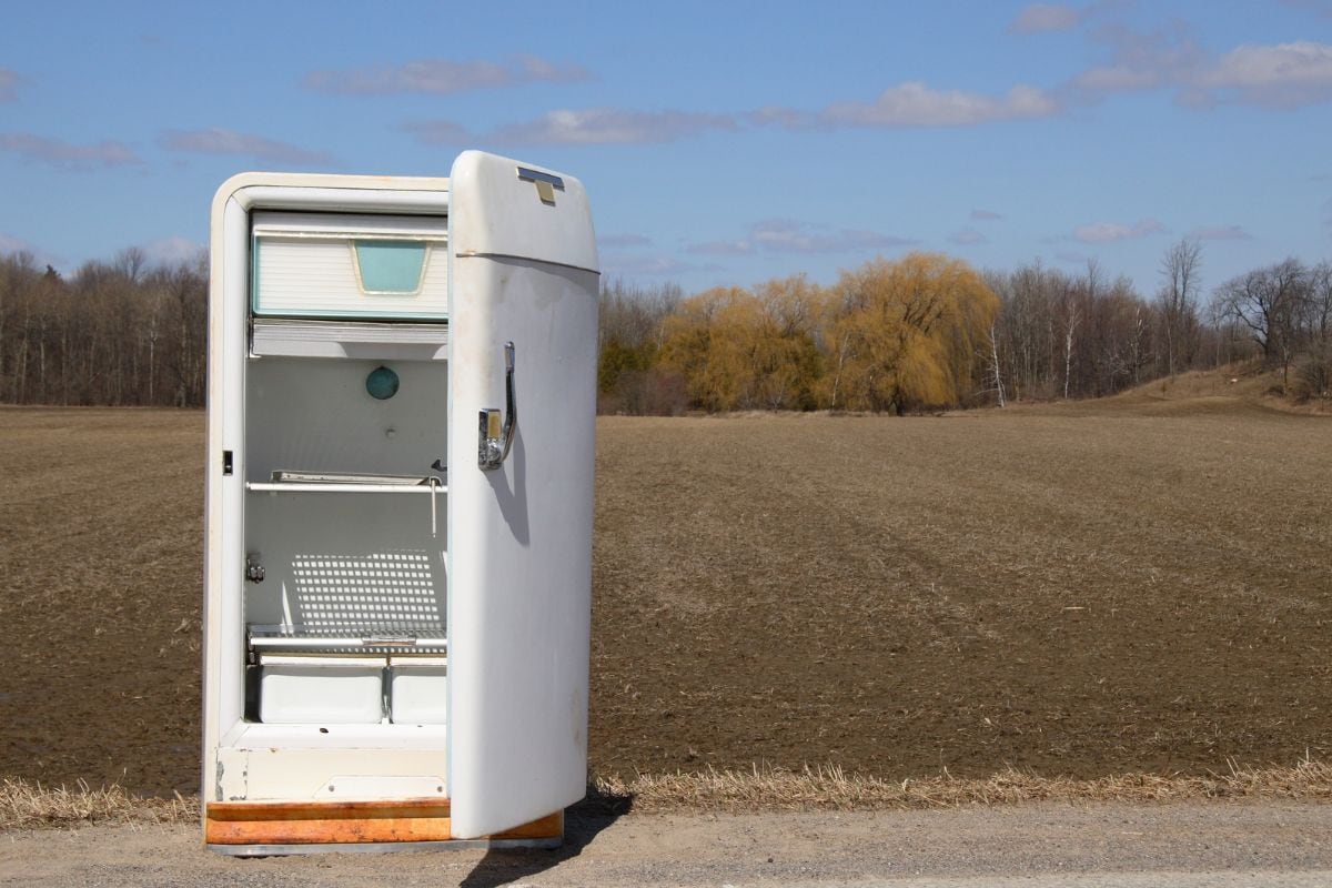 Old open fridge on roadside by farmers field.