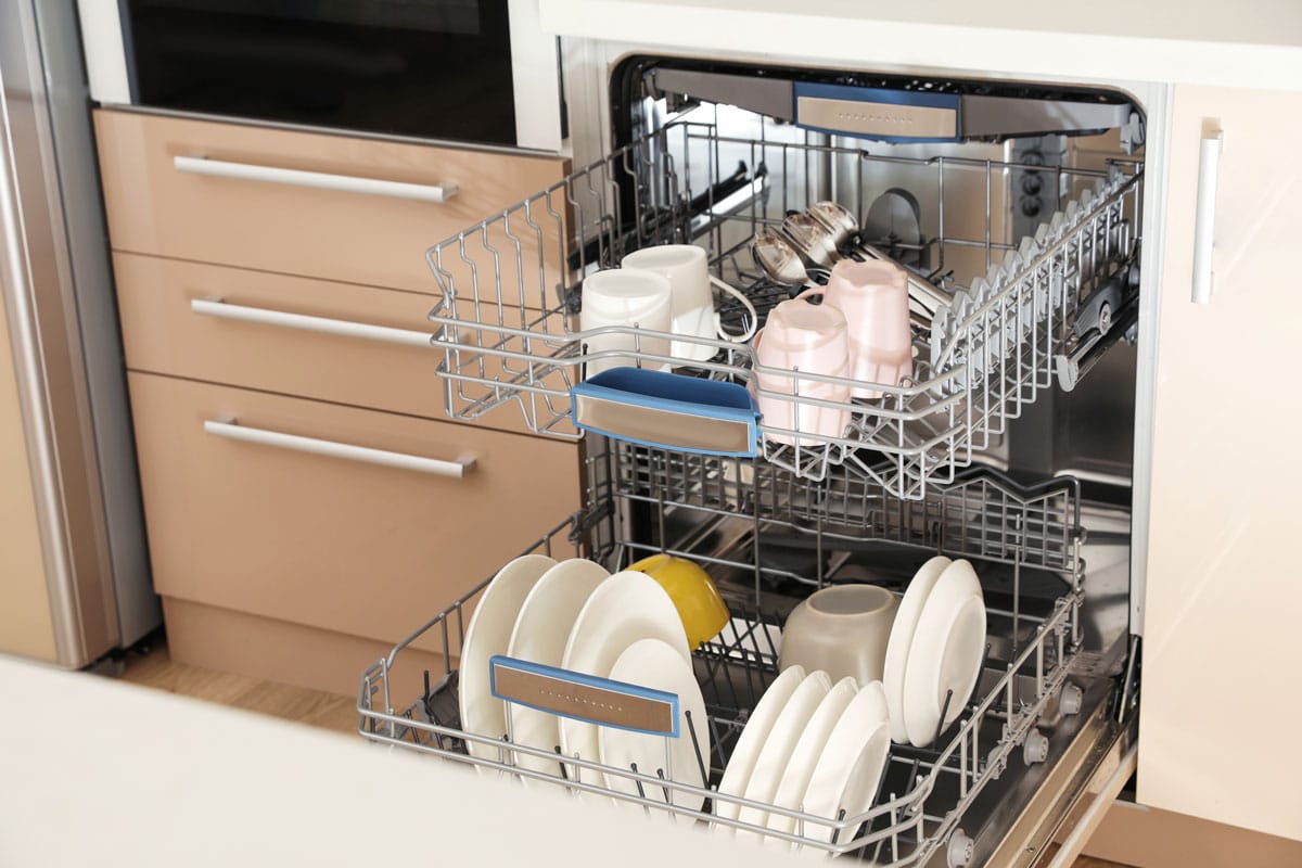 Open dishwasher with clean tableware in kitchen
